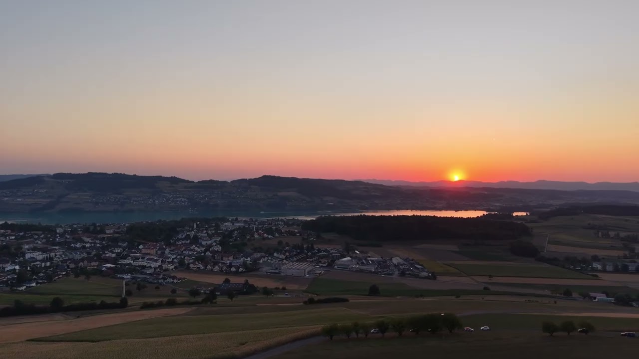 Luftaufnahme der tief stehenden Sonne über einem See, Dorf und Felder im Vordergrund