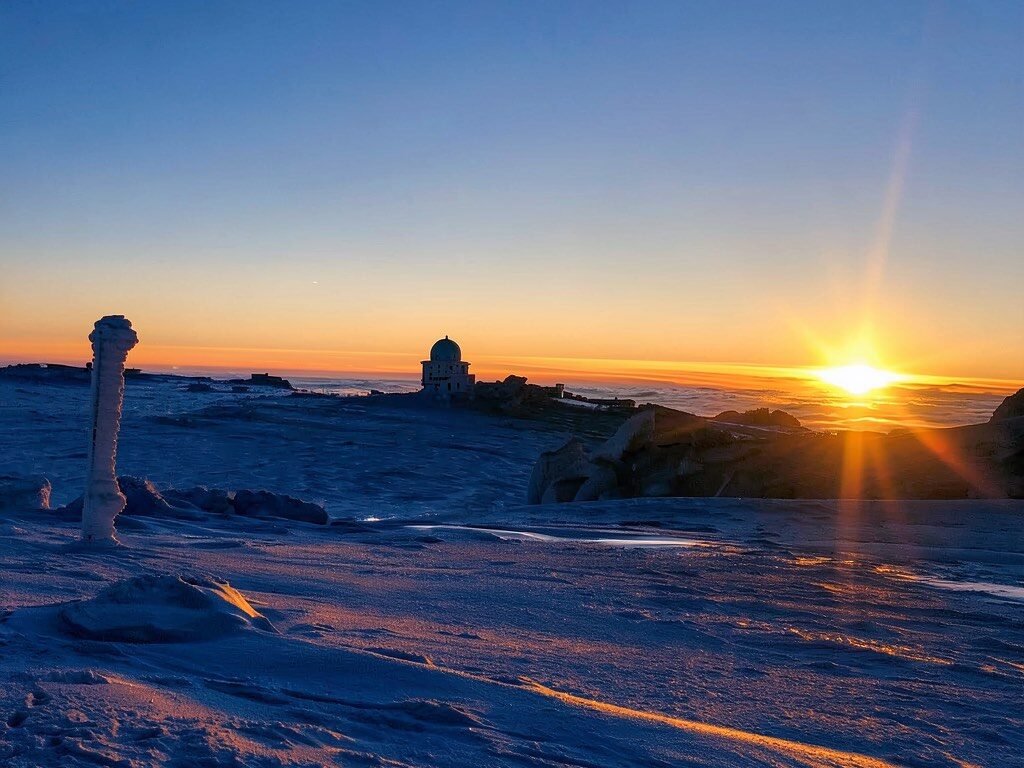 Verschneiter Gipfel mit Bergstation, Sonne über dem Nebelmeer